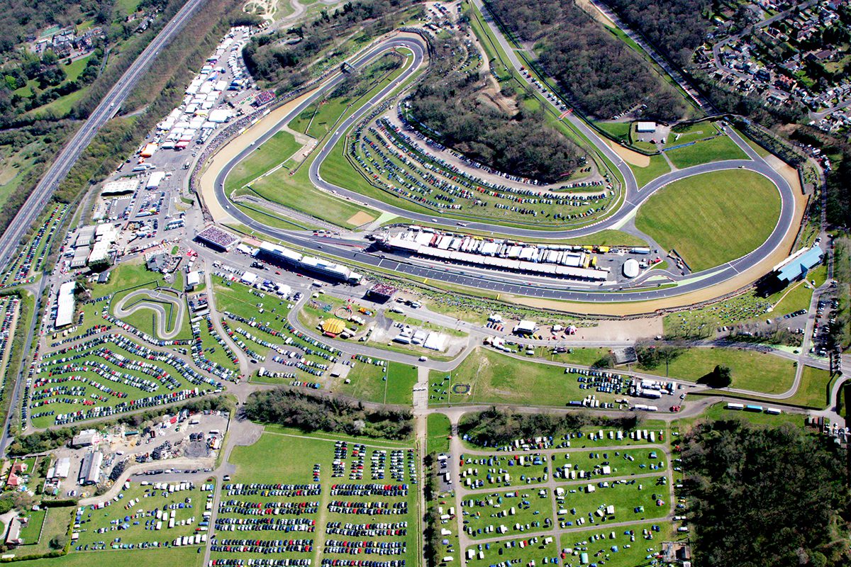 An aerial view of a race track with many cars parked in the grass.