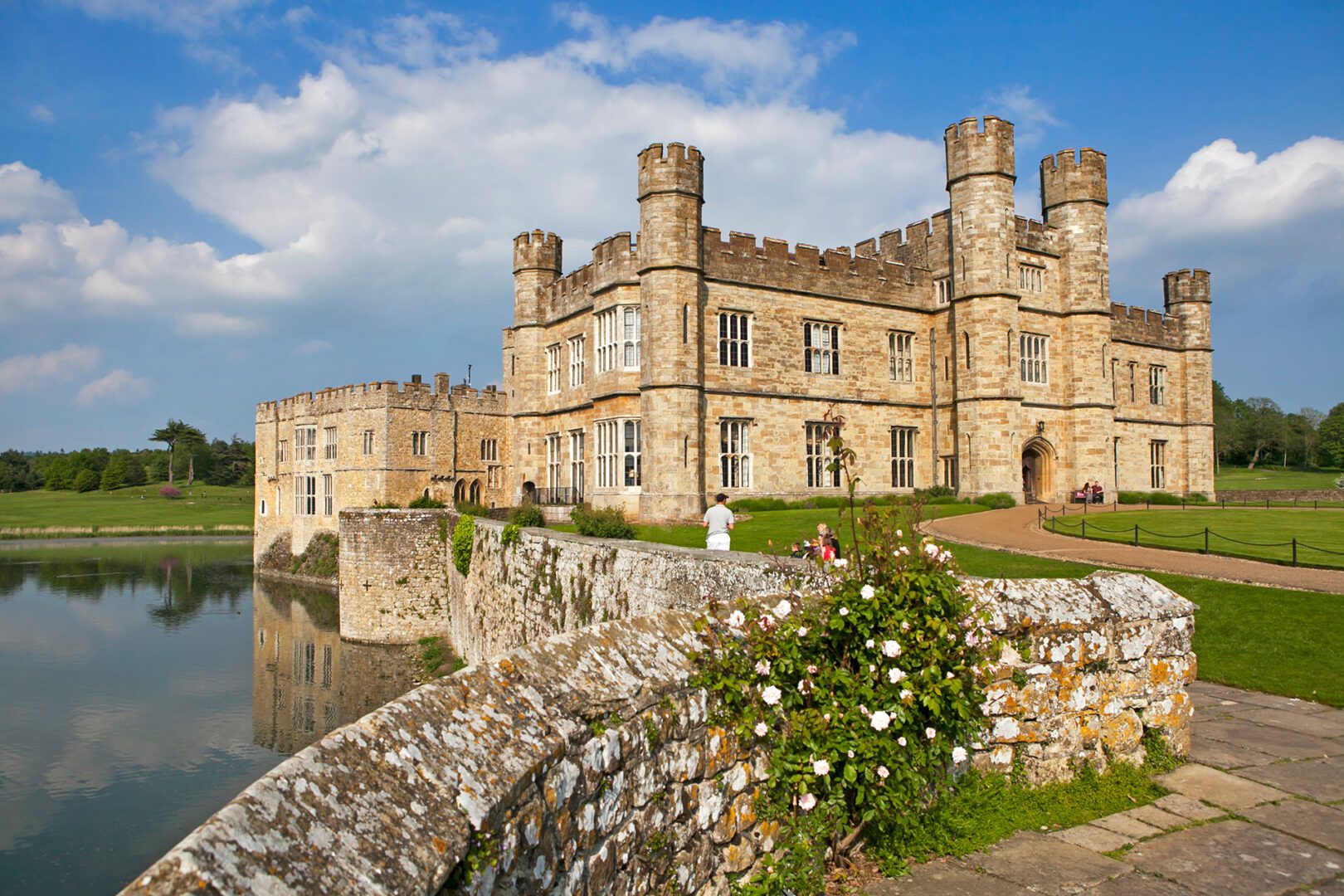 A castle with a pond and flowers in the foreground.