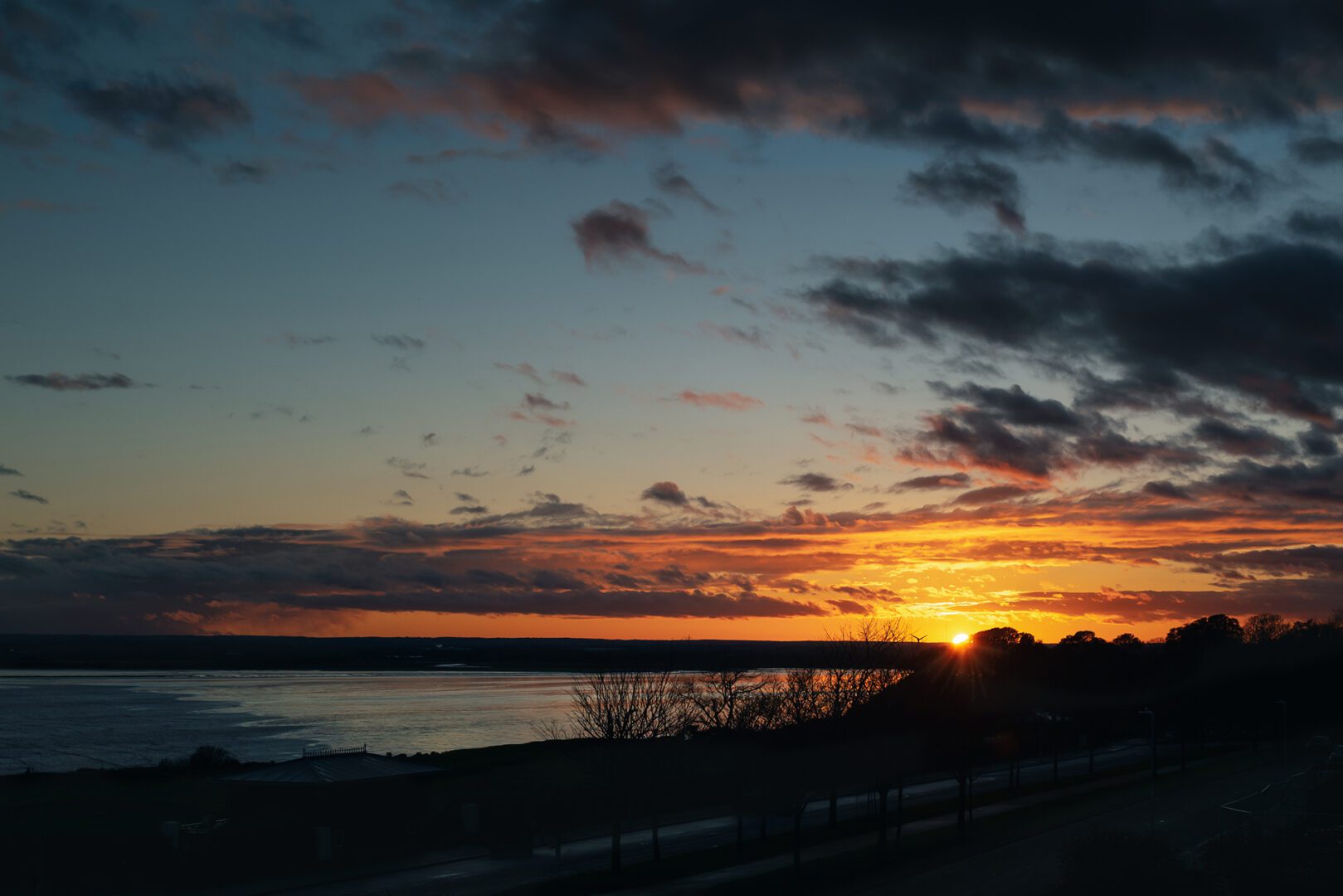 A sunset over the water with dark clouds in the sky.