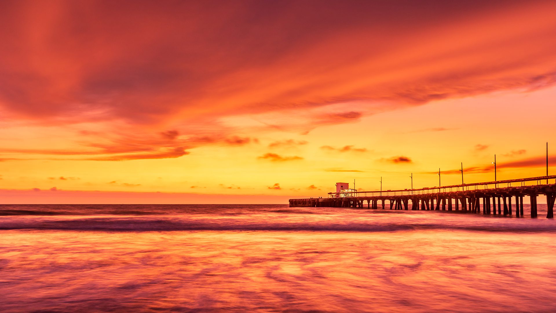 A pier is shown at sunset on the beach.