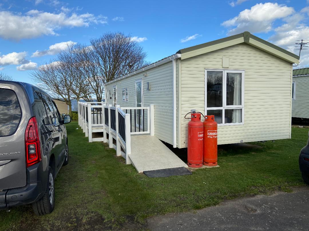 A white mobile home with red gas tanks and a car parked in front of it.