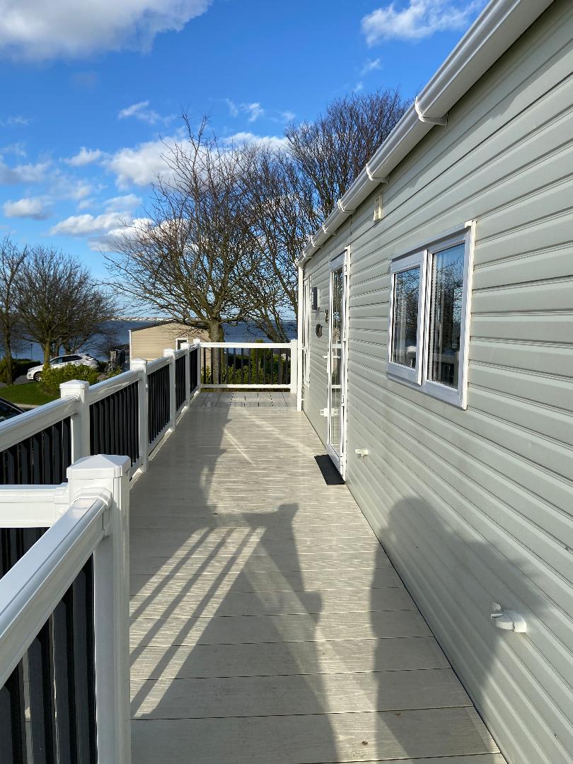 A white house with a deck and trees in the background.